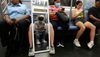 People sit on the subway with a full length mirror reflecting a person opposite them 