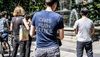 A person stands with their back to the camera in a blue t-shirt with writing on the back in yellow saying "Cars ruin cities"