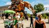 A paletas vendor and several tourists move through a street in Nantes as the Great Elephant mechanical art installation walks past them