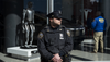 An officer from the New York Police department stands guard outside of a Tesla store window displaying a robot while another officer stands in the back of the frame investigating inside with 
