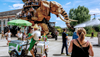 A paletas vendor and several tourists move through a street in Nantes as the Great Elephant mechanical art installation walks past them