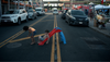 Two children play on a toy slide in the middle of a road lined with cars parked on the curb