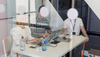Three people working on their laptops gather at a table in their office behind a glass wall with a row of four white dots imprinted on it; the dots obscure their faces