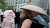 Two women in large, fancy hats exit the Frederick Law Olmstead Luncheon at the Central Park Conservancy; one walks towards a car with her back to the camera, the other is shown in profile loo