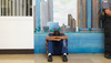 An inmate at the Michigan Reformatory sits crouched with his head bent down in his arms in front of a painted backdrop of a city and a window with bars; a corrections officer is seen standin