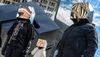 Three people stand in front of the Astor Place cube wearing metallic cubes on top of their heads