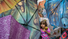A young girl holding a caramel apple stands amidst a display of umbrellas featuring famous artworks and colorful patterns
