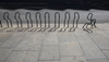A row of bike racks on a city sidewalk, the rightmost rack twisted out of shape