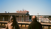 Two people stand on the platform of the above-ground 20 Avenue subway station looking at a high-rise apartment being constructed in the distance