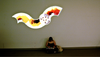Person sits cross-legged on the floor reading beneath a glowing wavy wall artwork