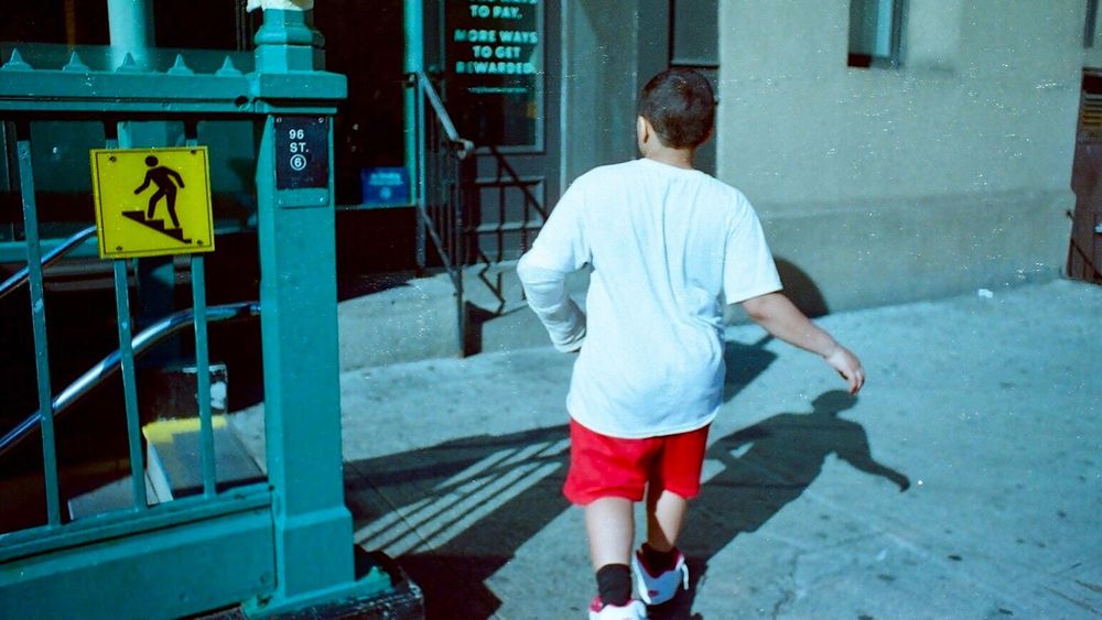 Closeup of a boy approaching the 96th Street New York City subway entrance from the sidewalk.