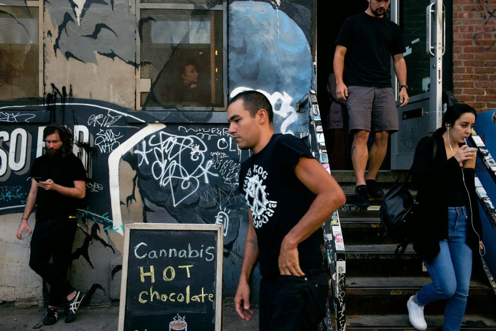 People walk past a chalkboard sign advertising cannabis hot chocolate