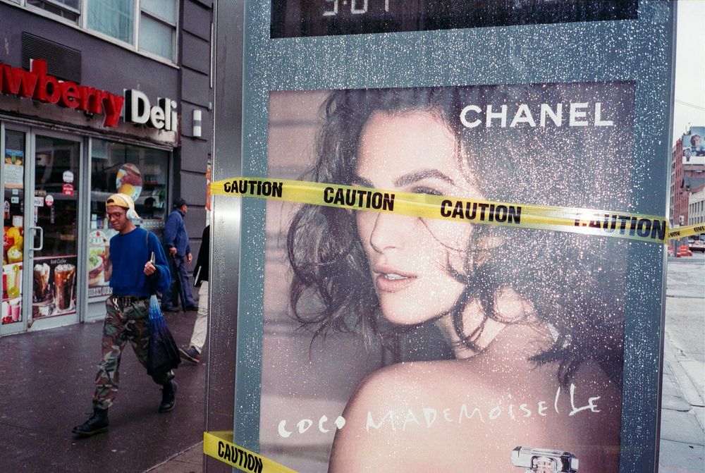 A man walks by a bus stop displaying a Chanel ad with caution tape wrapped across it