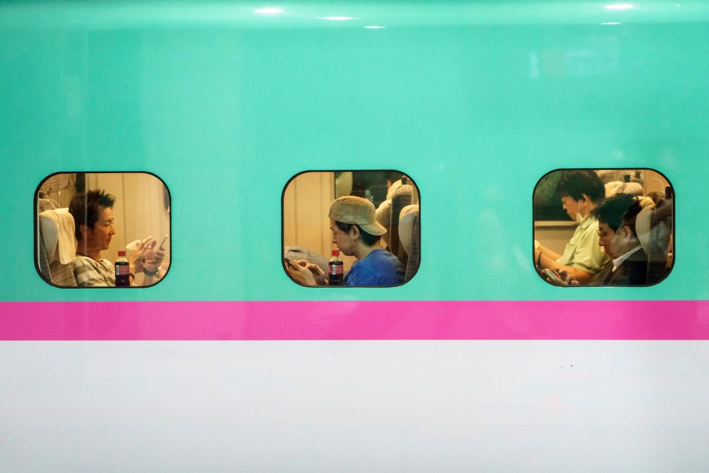 Three passengers are seen through three separate windows in a Japanese commuter train car