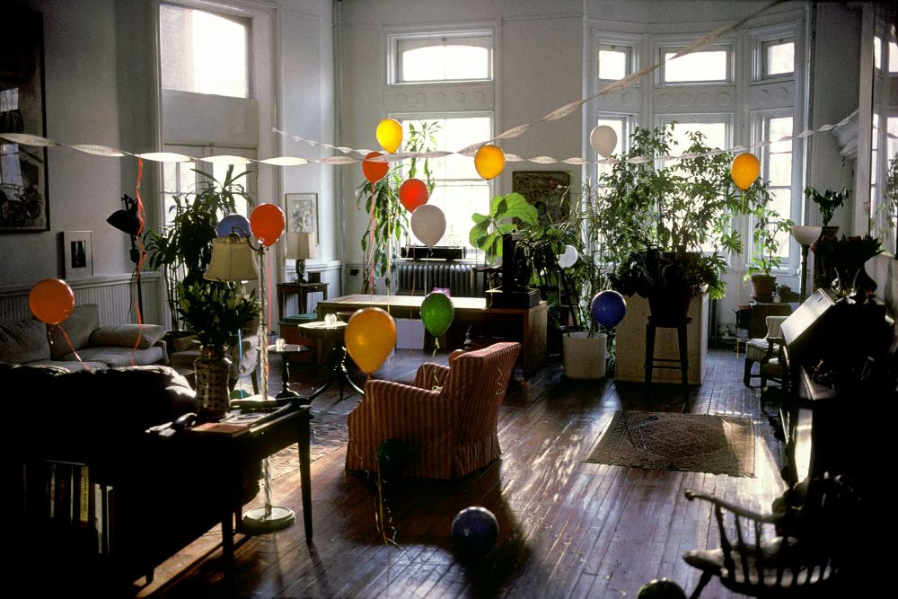 An apartment decorated with antique furniture and large plants is filled with colorful balloons