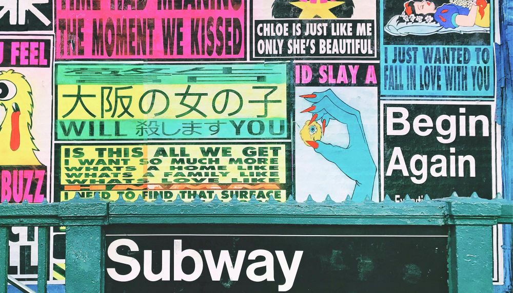 An image of a subway entrance with colourful graffiti style posters behind it on the wall