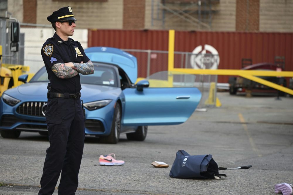 A police officer stands near a car, a shoe and bag on the ground