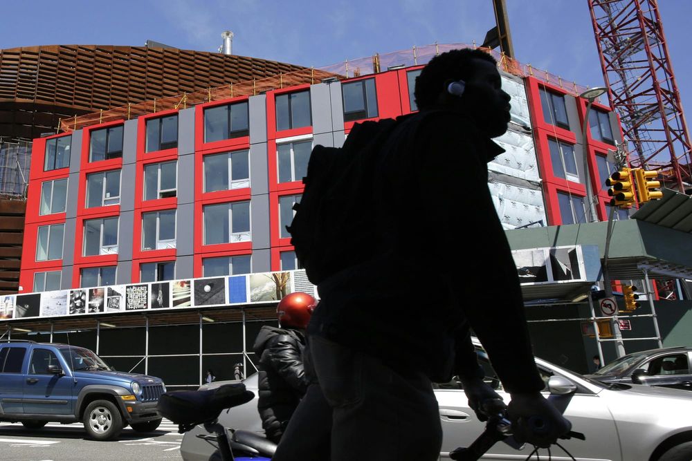 A cyclist passes a red and gray modular apartment building under construction