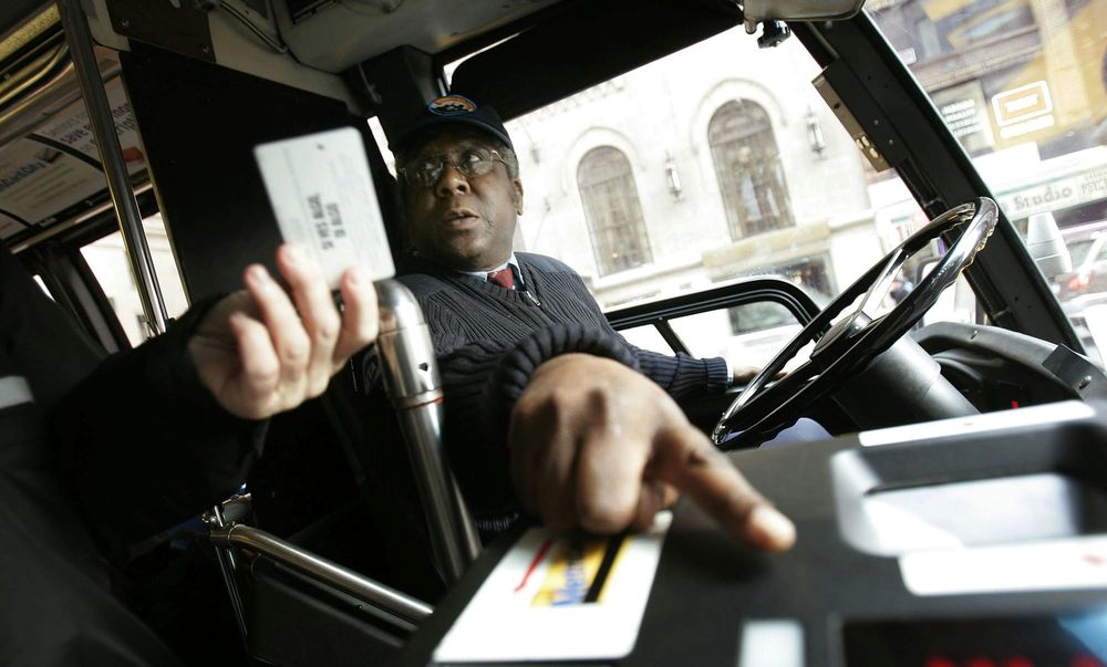 A bus driver reaches out from the driver’s seat holding a card