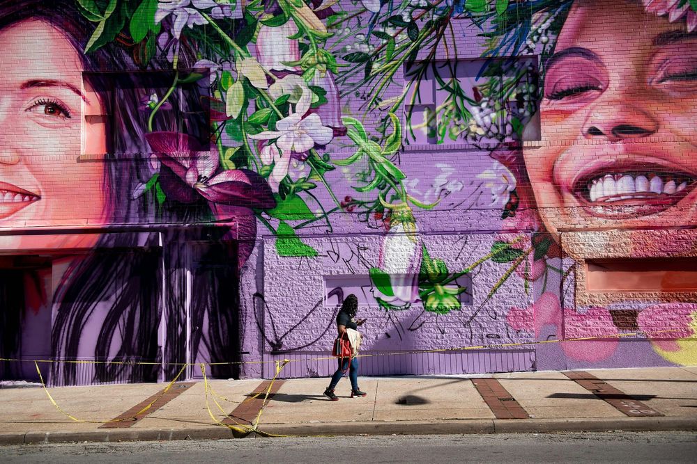 A woman walks past a wall mural of two smiling faces