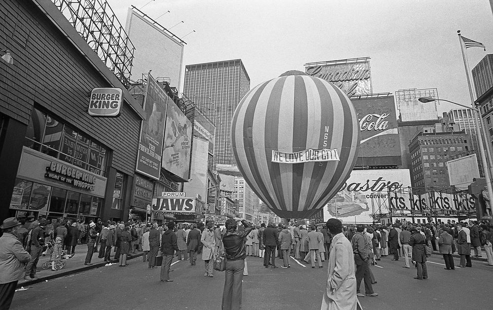 A striped hot air balloon reading We Love Our City floats over Times Square