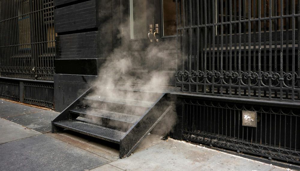 Steam rises from a building’s basement stairwell on a sidewalk