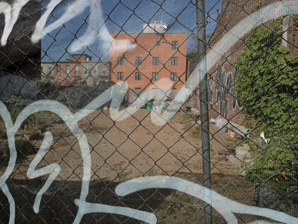 Houses and a vacant lot seen through a graffiti-covered chain-link fence