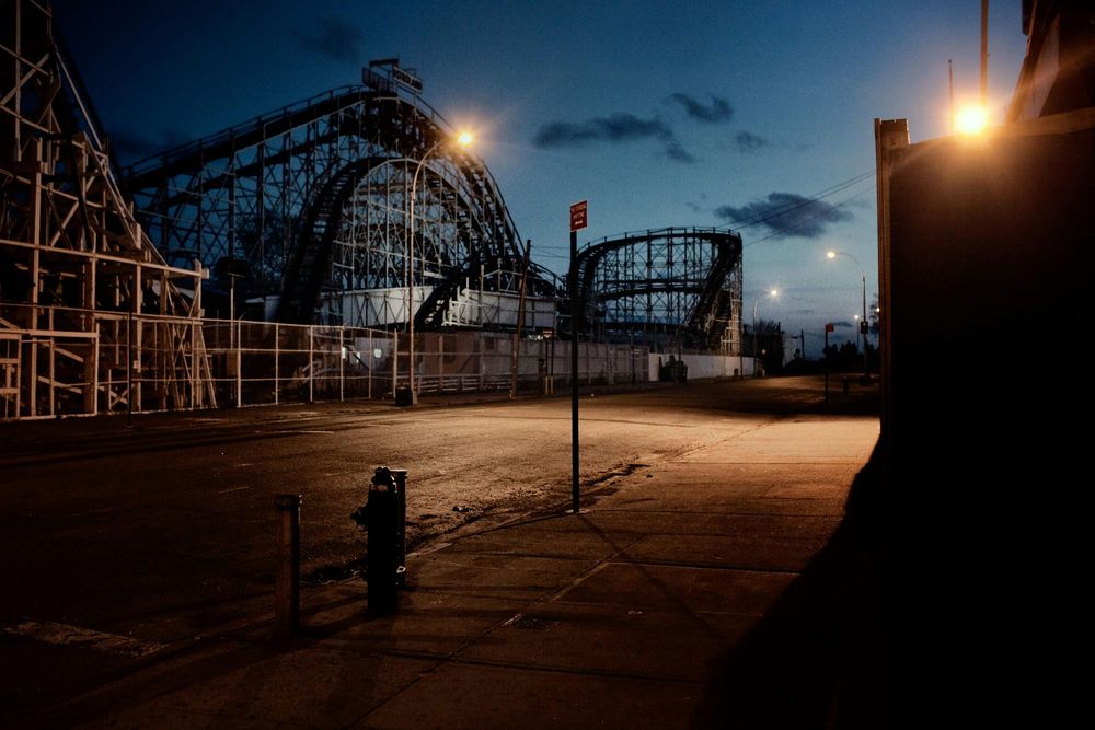 An empty street at dusk with a roller coaster silhouette behind it