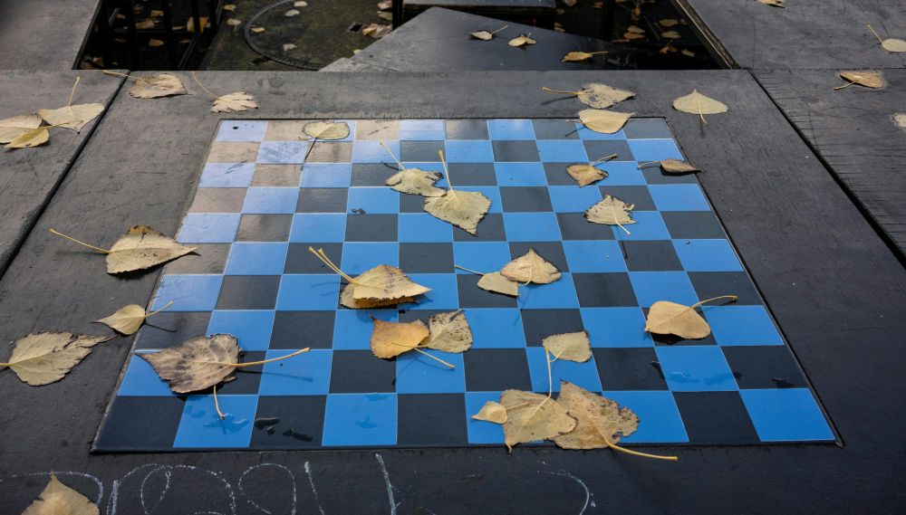 A checkerboard table in blue and black scattered with fallen leaves