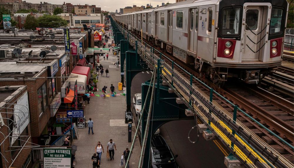 A train on an elevated subway line passes shops and pedestrians on Roosevelt Avenue in Corona, Queens