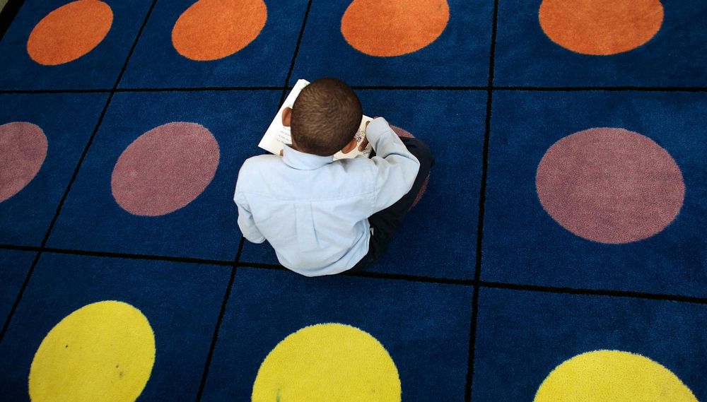 A boy sits alone reading on a polka-dot classroom rug