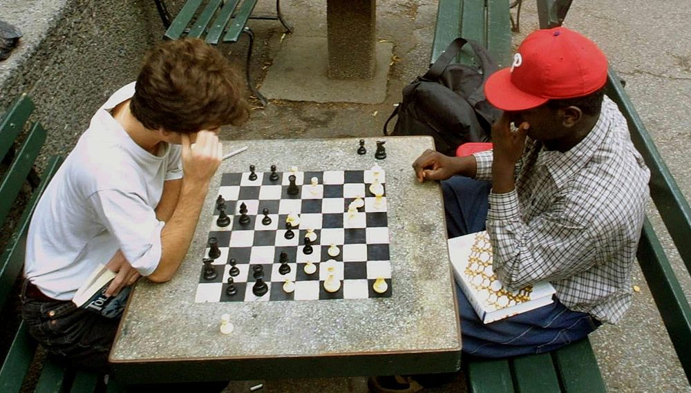 Two boys play chess at a park table