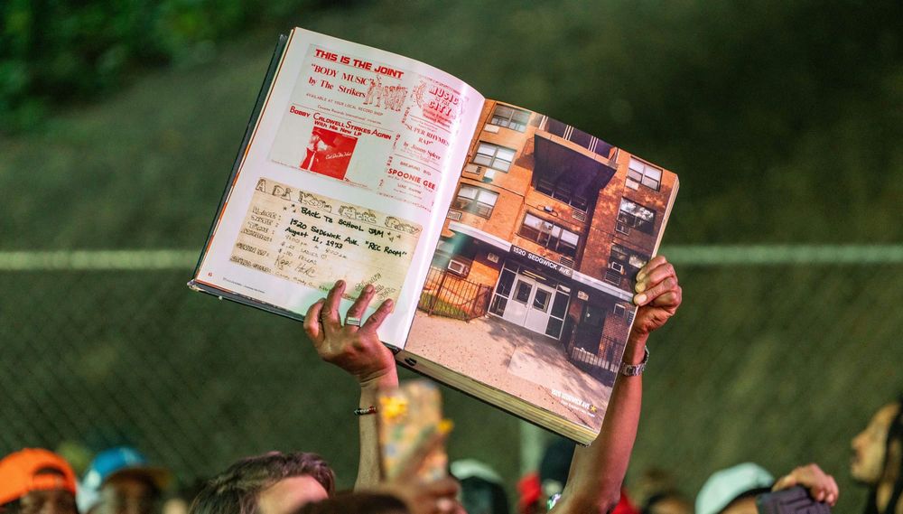 A person holds up a photo of 1520 Sedgwick Avenue and the flier for the first hip-hop jam during a celebration for the fiftieth anniversary of hip-hop on August 12, 2023 in The Bronx borough