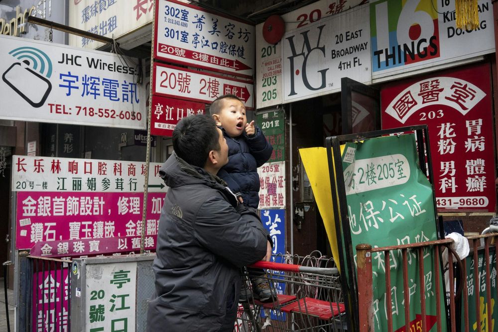 A man holding a baby outside of a storefront covered in signs written in multiple languages
