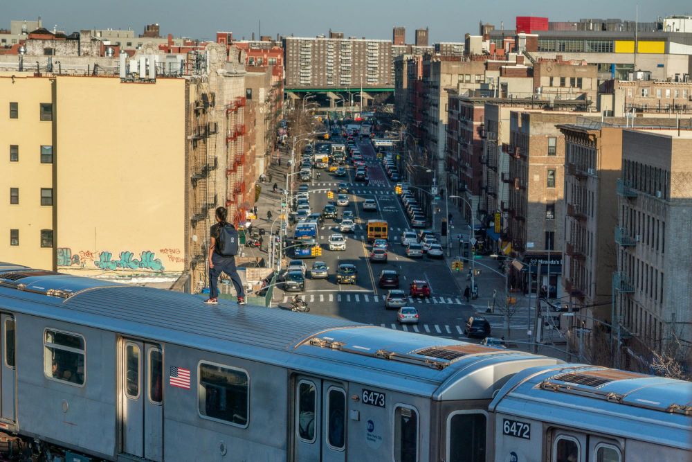 A man walking on top of an above ground subway train overlooking a Bronx street