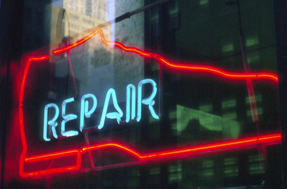 A red neon sign in the shape of a dress shoe with the word "repair" written in light blue neon within it