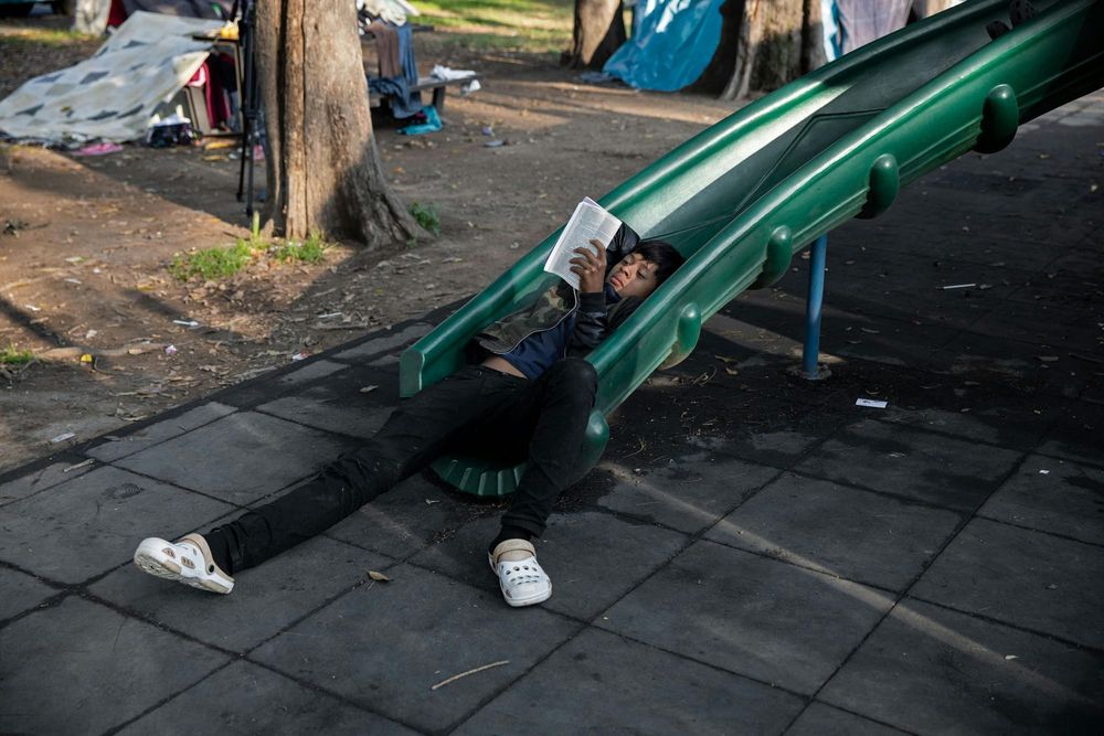 A child reads a book while lying on a green slide at a playground