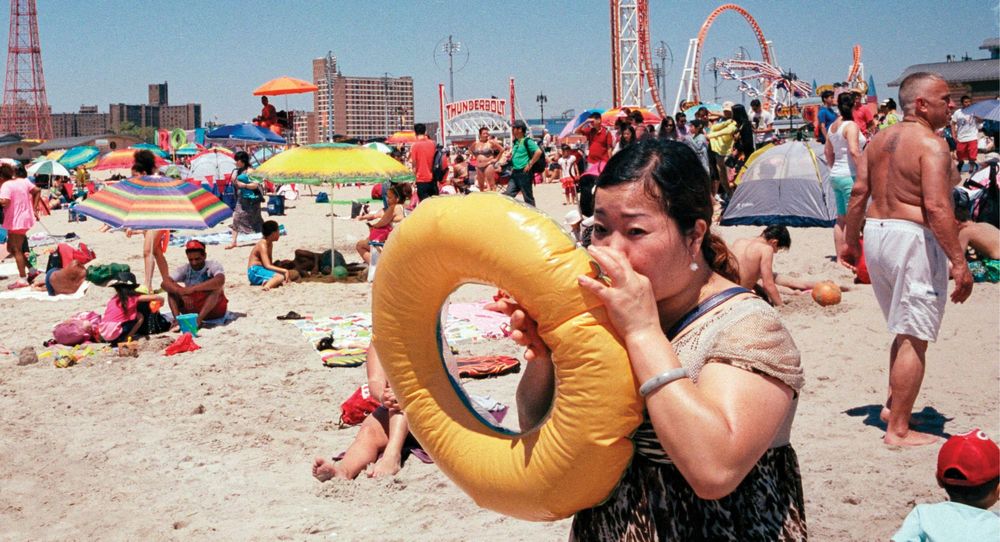 A woman blowing up a round yellow pool float on a crowded beach