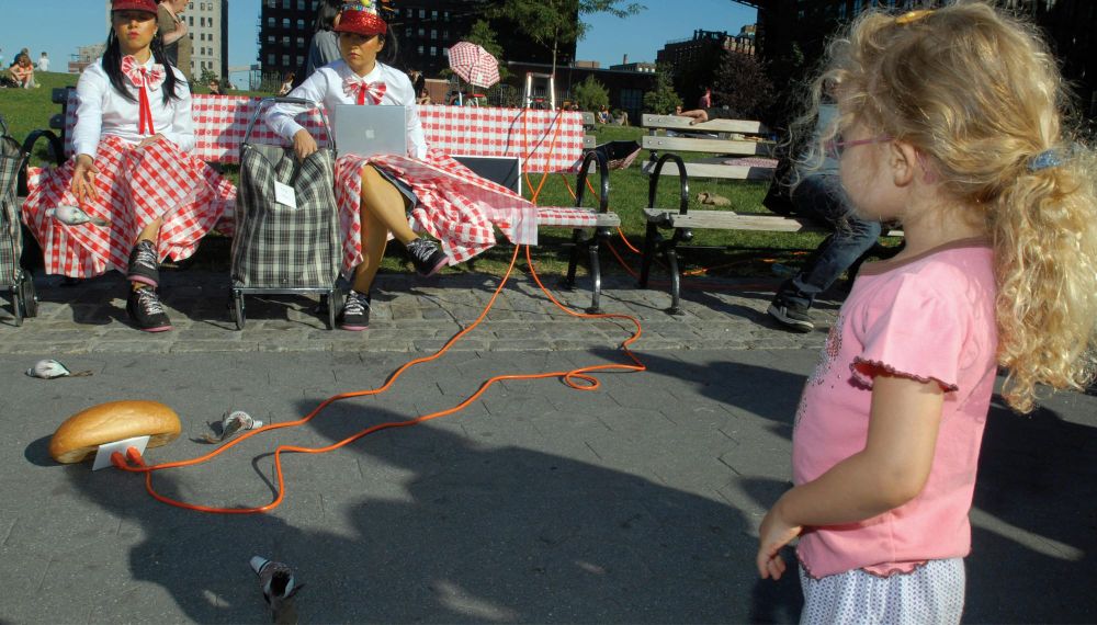 The performance art duo The Disorientals performs a piece involving a battery powered loaf of bread in Brooklyn Bridge Park as a young girl looks on