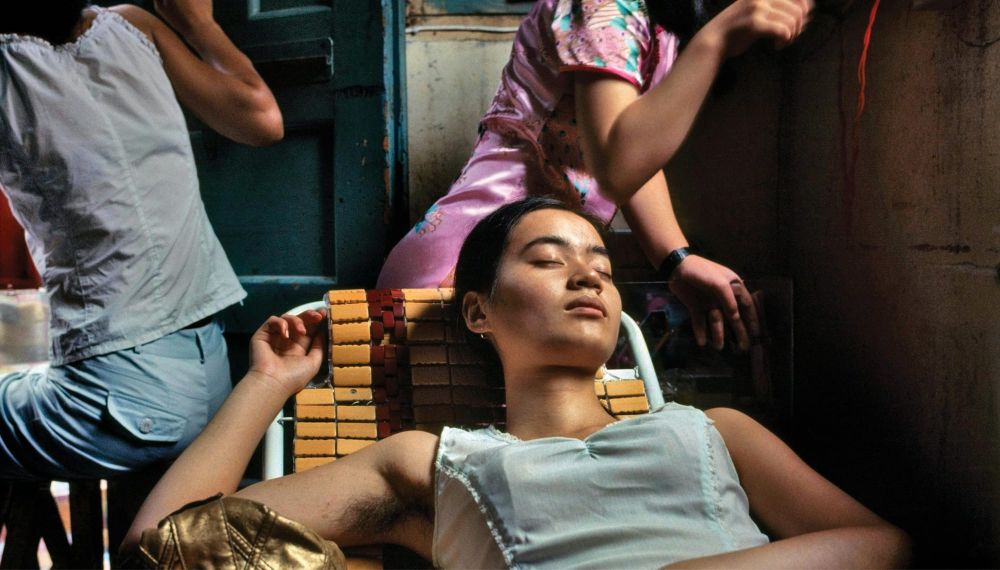 A woman lounges with her eyes closed on a lawn chair inside a restaurant with two other figures in the background