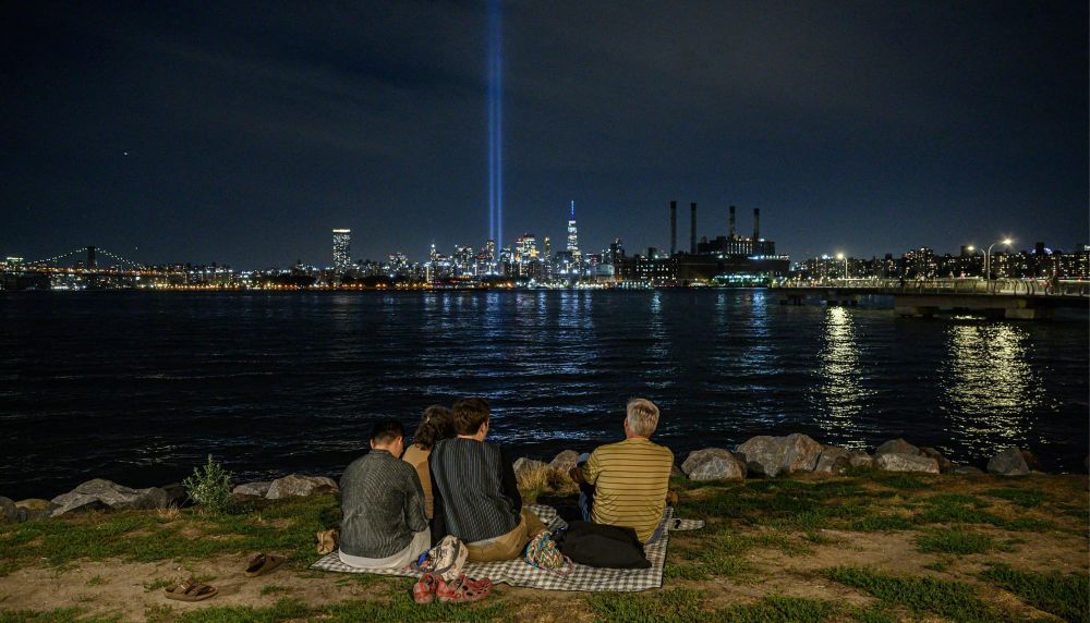 4 people look at the New York skyline at night over the water
