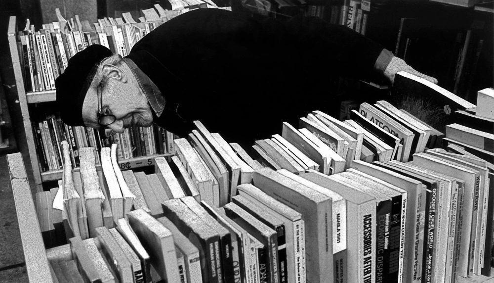 Elderly man leans down to look at library shelf