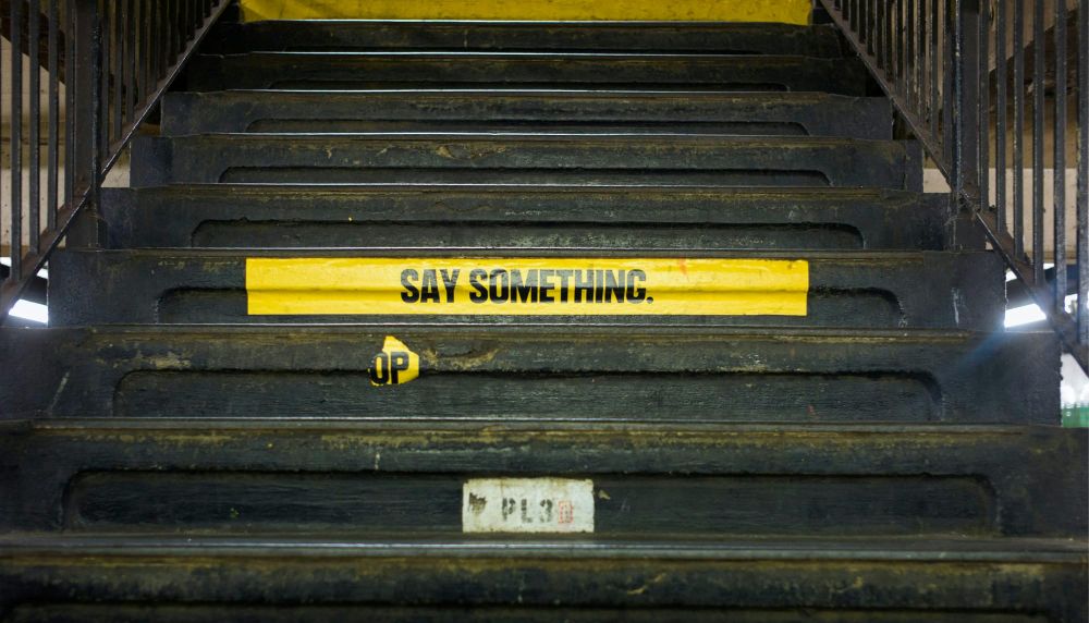 Dark subway stairs with yellow sign that reads "SAY SOMETHING"