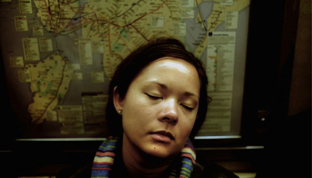 Woman riding the subway with closed eyes, a subway map behind her