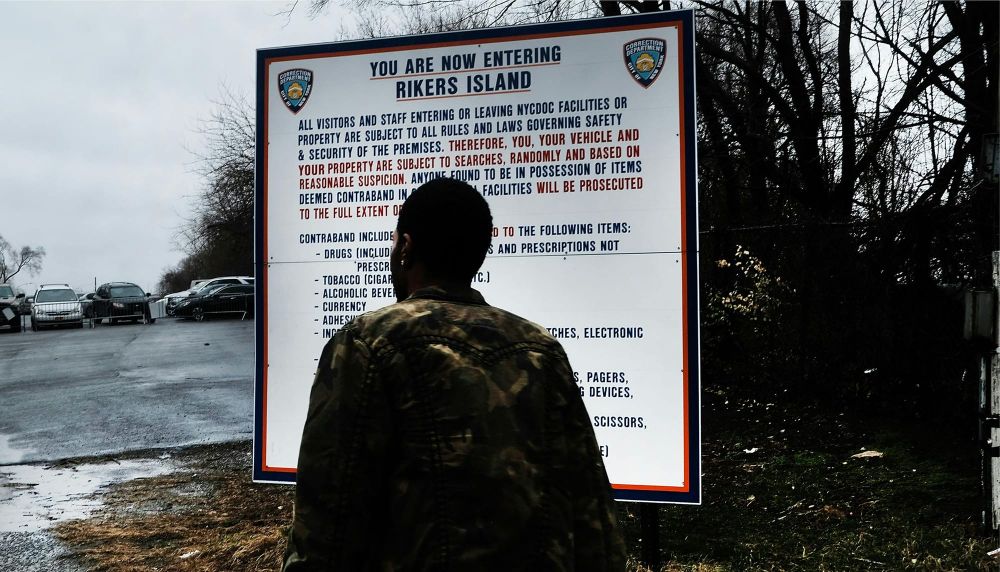 Back shot of a person facing a sign entitled "you are now entering Rikers Island"