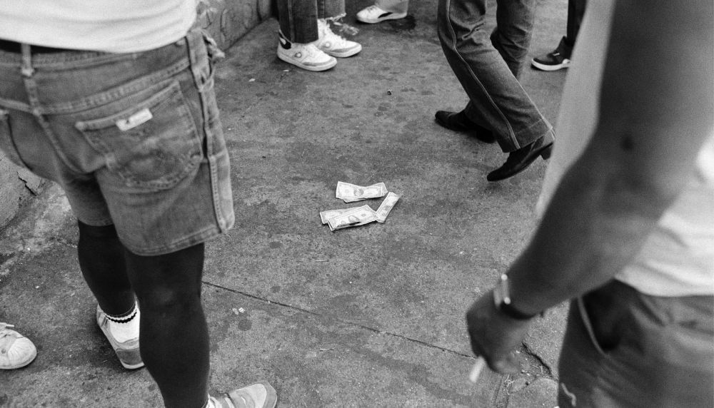 Black and white shot of money on the floor surrounded by people's legs