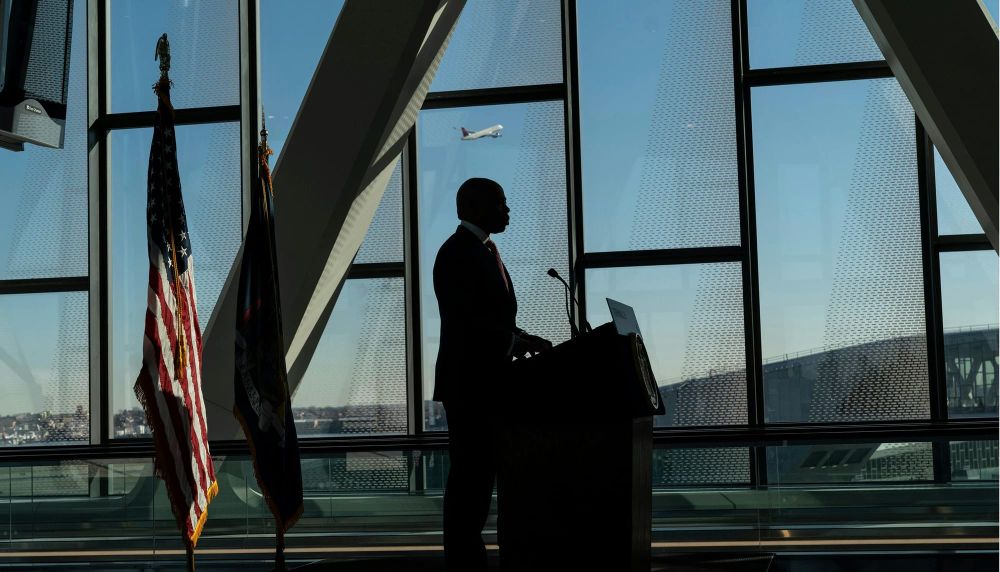 Mayor Eric Adams speaks while airplane seen through the window departs airport.