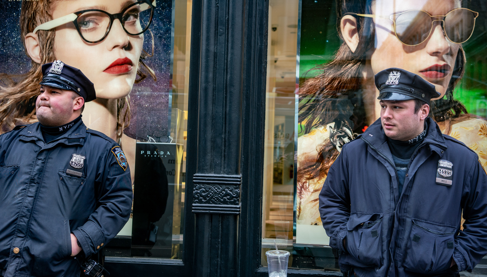 Two policemen stand in front of a store displaying ads for glasses in the window