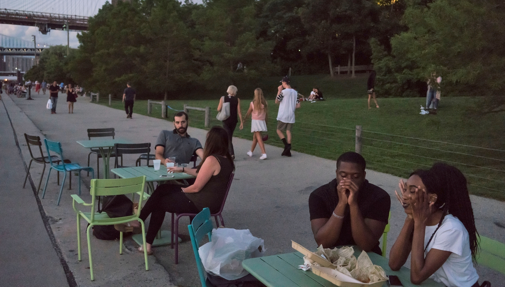 Two couples sit at tables along the waterfront at Brooklyn Bridge Park