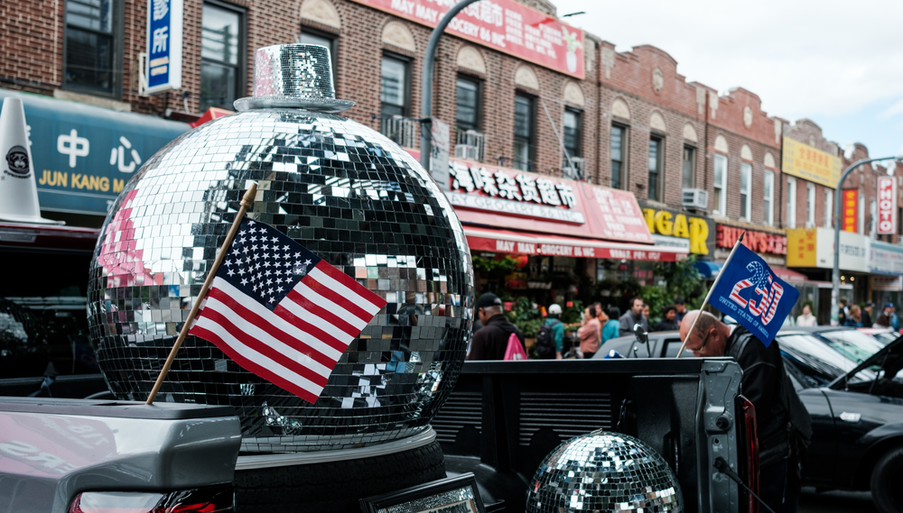 A giant disco ball is displayed on a a parade float next to an American flag on a block in Sunset Park, Brooklyn